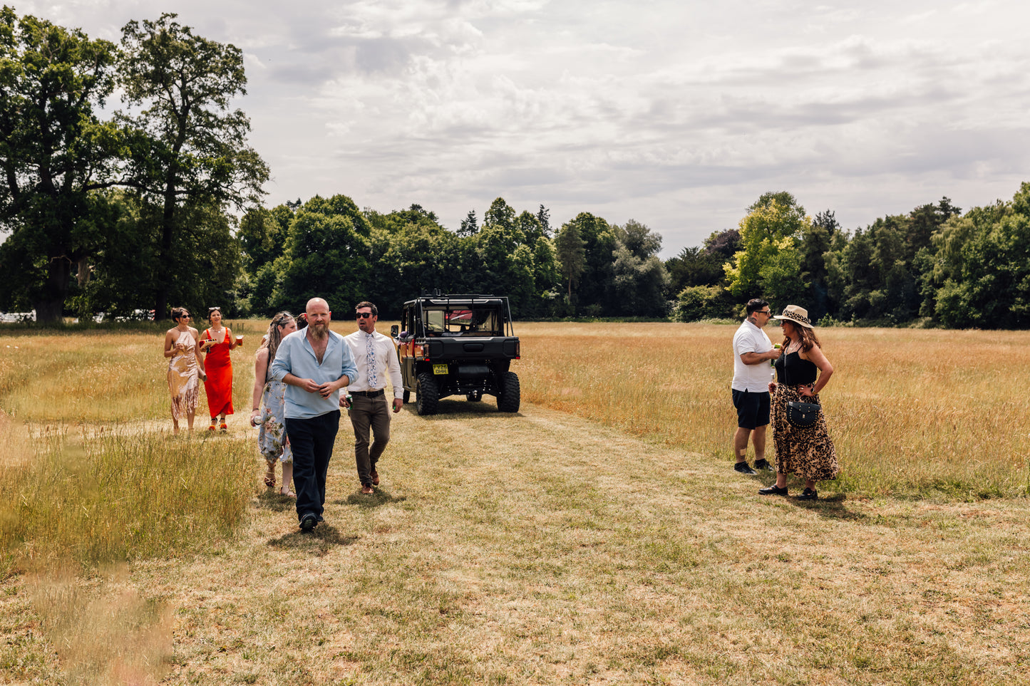 Group of people walking on a dirt path through a field with CFMOTO UTV in the background