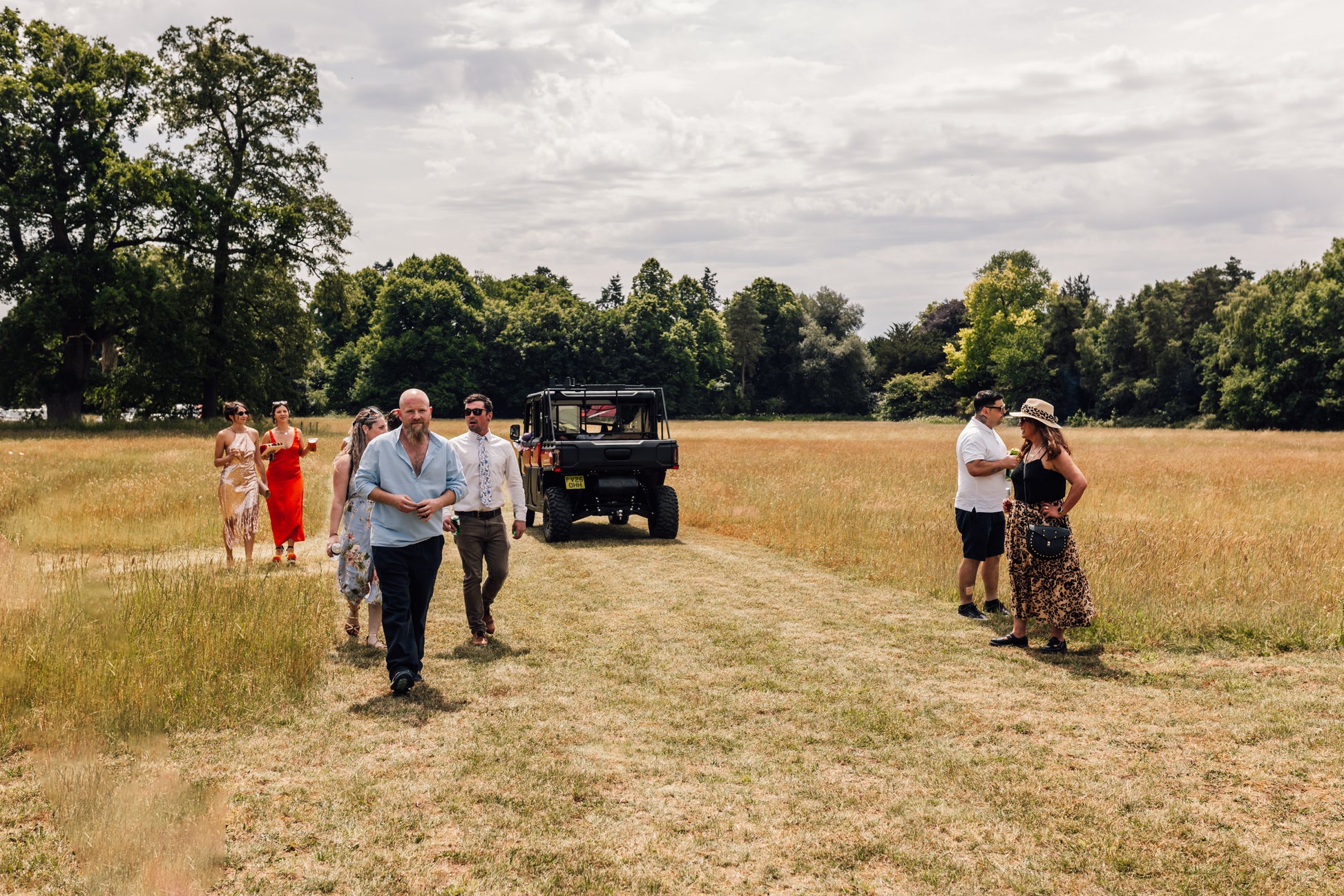 Group of people walking on a dirt path through a field with CFMOTO UTV in the background