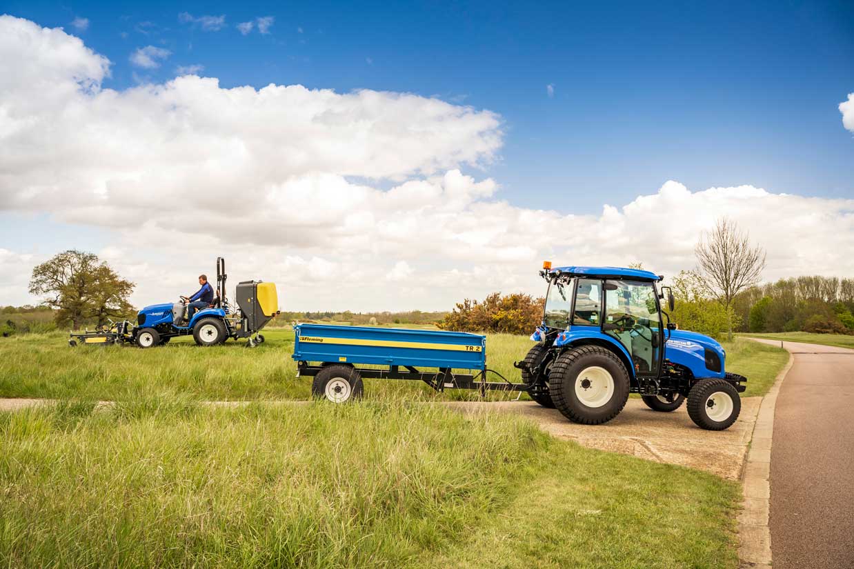 A tractor with a Fleming tractor tipping trailer on a grassy field under a blue sky with clouds.