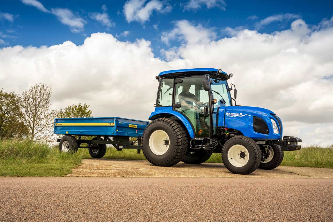 Blue tractor with a Fleming tractor tipping trailer on a road under a blue sky with clouds