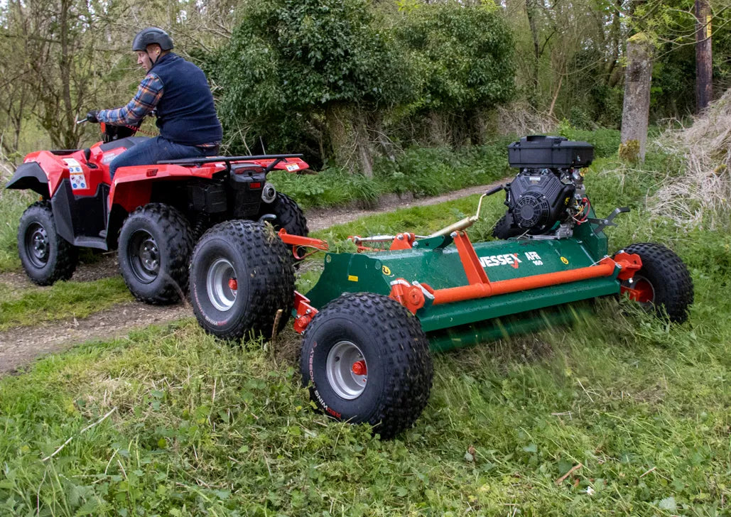 Person operating a red ATV pulling a Wessex ATV flail mower through grass and trees.