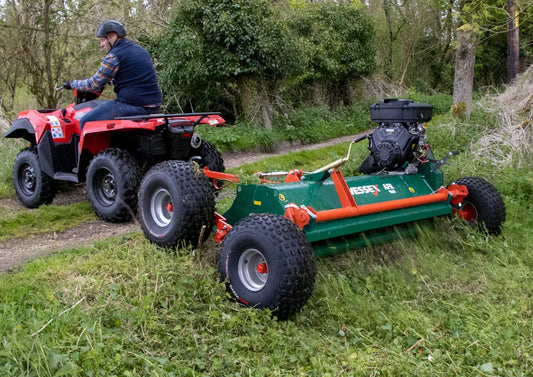 Person operating a red ATV pulling a Wessex ATV flail mower through grass and trees.