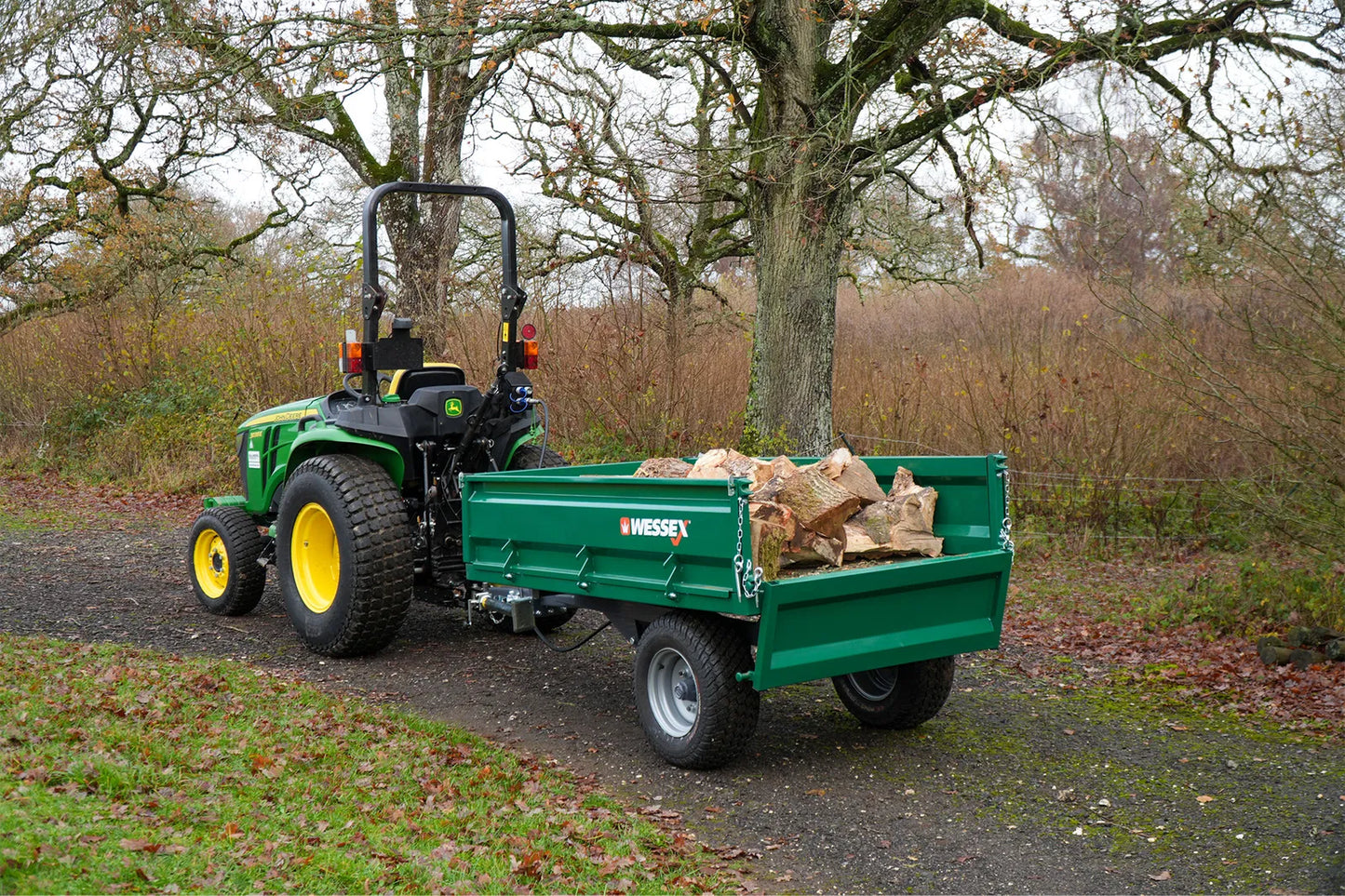 Green tractor with a Wessex tipping tractor trailer carrying logs in a wooded area