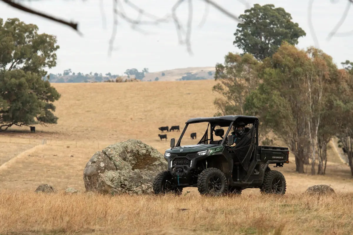 Green CFMOTO utility vehicle in a field with trees and hills in the background