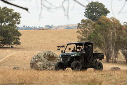 Green CFMOTO utility vehicle in a field with trees and hills in the background