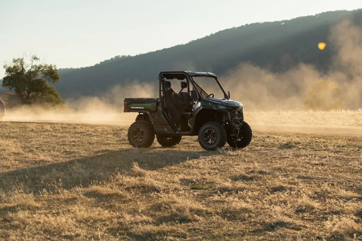 Green CFMOTO U10 Pro utility vehicle driving on a dirt road with mountains in the background