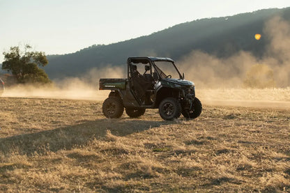 Green CFMOTO U10 Pro utility vehicle driving on a dirt road with mountains in the background