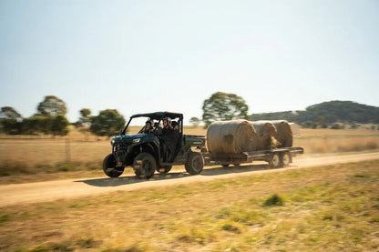 CFMOTO U10 Pro UTV with a trailer carrying hay bales on a dirt road in a rural setting.
