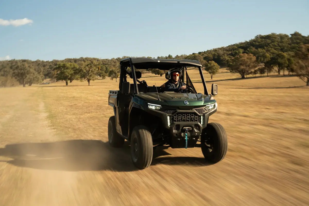 Person driving a CFMOTO U10 Pro utility terrain vehicle on a dirt road with trees in the background