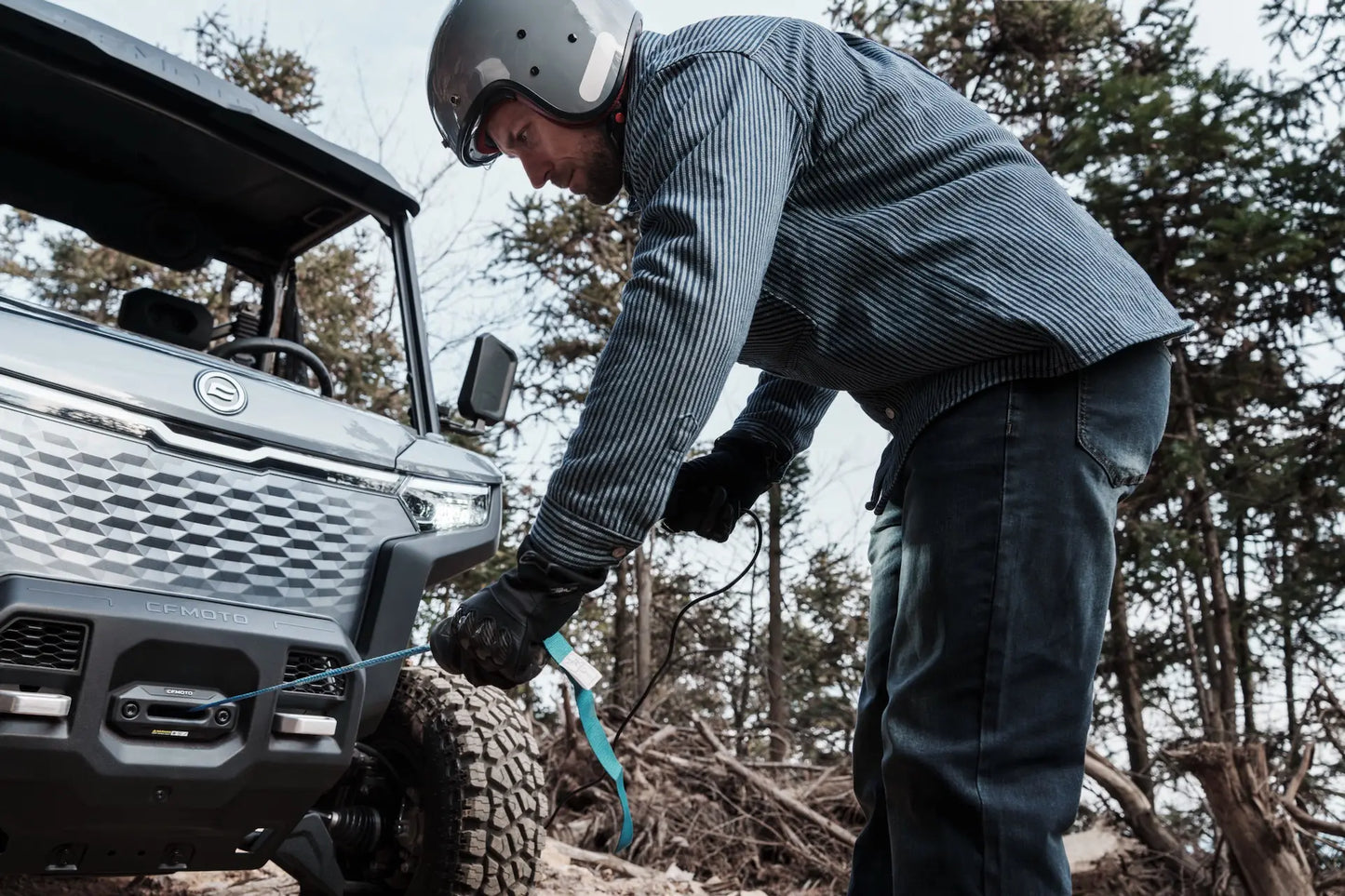 Person in a helmet and gloves working with a CFMOTO U6EV Electric UTV winch in a forest setting