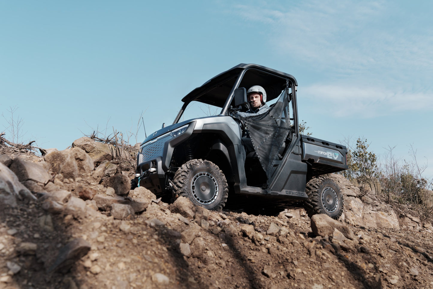 Person driving a CFMOTO U6EV Electric UTV on rocky terrain with a clear blue sky.