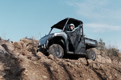 Person driving a CFMOTO U6EV Electric UTV on rocky terrain with a clear blue sky.