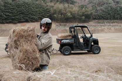 Person lifting a hay bale with a CFMOTO U6EV Electric UTV in the background