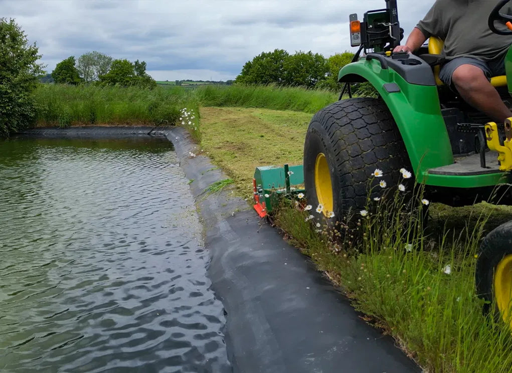 Person operating a Wessex Flail Mower near a body of water with grass and trees in the background.