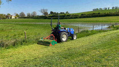 Tractor mowing a field with a pond and trees in the background