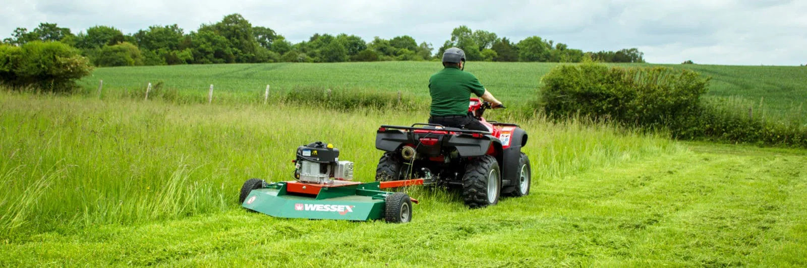 Person operating a Wessex ATV topper mower attached to an ATV in a grassy field.
