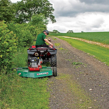 Person operating a Wessex ATV topper mower on a gravel path with greenery around