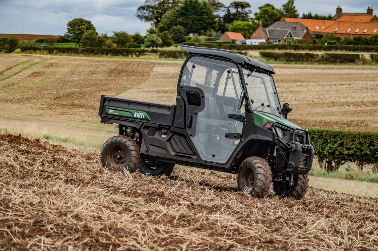 Kioti UTV utility vehicle in a field with a rural landscape in the background.