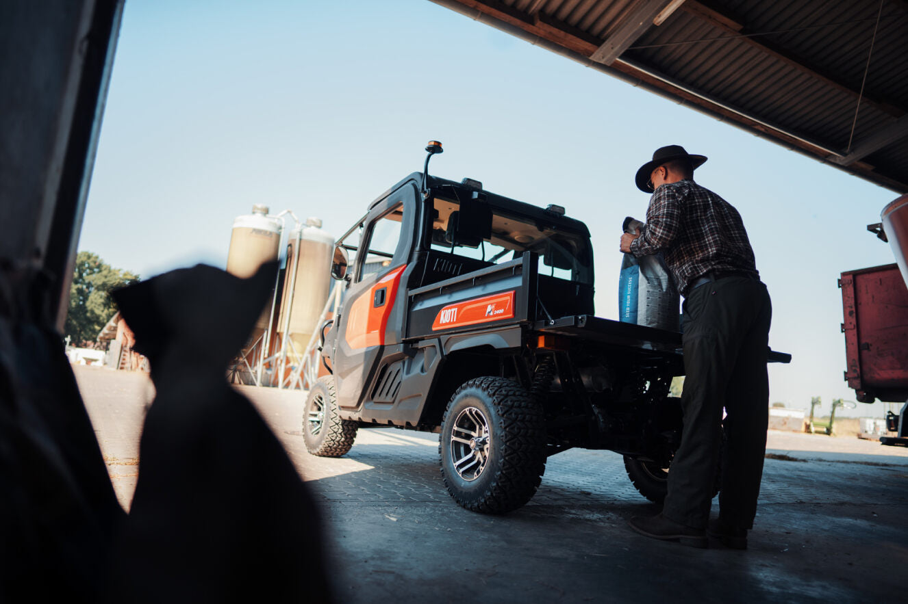 Person loading a large container into a Kioti K9 utility vehicle under a sheltered area.