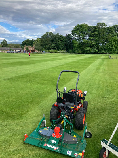 Golf course with a wessex mower on a green field under a cloudy sky.
