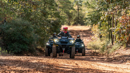 Three people riding Can-Am ATVs on a dirt road through a forest