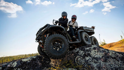 Two people on a Can-Am Outlander 6x6 ATV in a natural landscape with a clear sky.