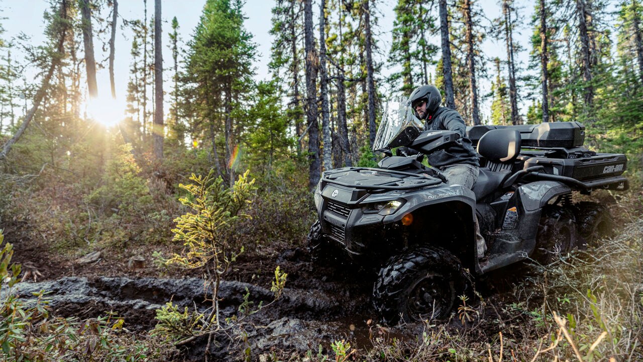 Person riding a Can-Am 6x6 ATV through a forest with trees and sunlight in the background