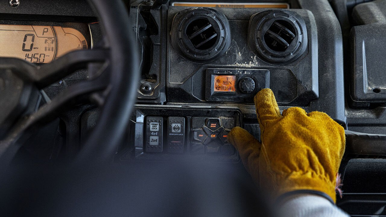 Hand wearing a yellow glove operating controls on a Can-Am UTV's dashboard.