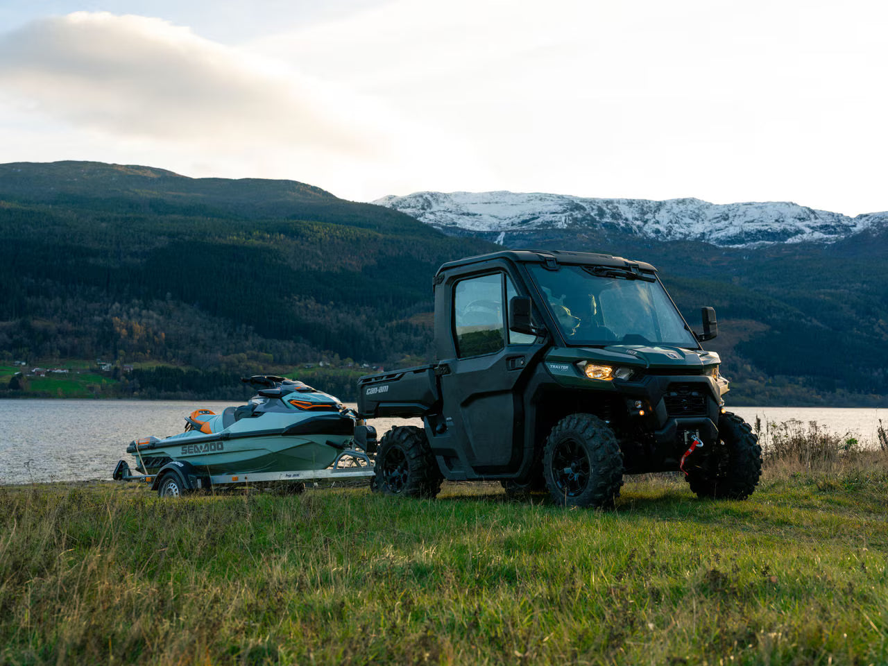 Can-Am UTV towing a boat on a grassy area with mountains in the background