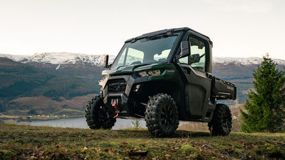 Green Can-Am off-road vehicle on a grassy area with mountains and trees in the background
