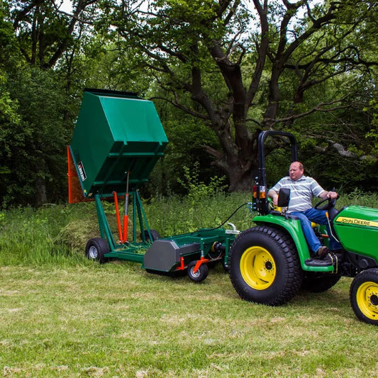 Man operating a green John Deere tractor with a Wessex flail collector attached in a grassy outdoor setting.