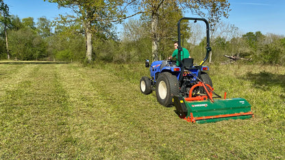 Tractor with a Wessex Flail Mower attachment mowing grass in a field with trees in the background