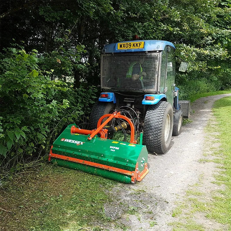 Tractor with a Wessex Flail Mower attachment on a path surrounded by trees